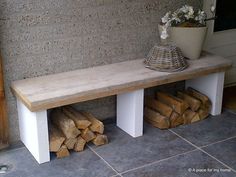 a wooden bench sitting on top of a pile of firewood next to a potted plant