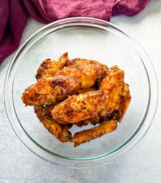 a glass bowl filled with chicken wings on top of a white countertop next to a pink towel