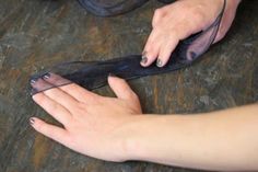 a woman's hands holding onto a piece of black sheer fabric on the floor