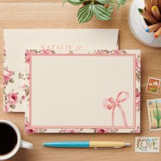 an envelope with a pink ribbon on it next to some stamps and a cup of coffee