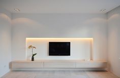 a white living room with a flat screen tv on the wall and some flowers in a vase