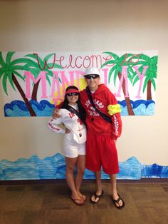 a man and woman standing next to each other in front of a welcome sign with palm trees