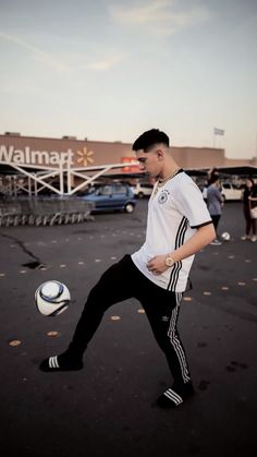 a young man kicking a soccer ball on top of a parking lot