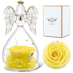 an angel figurine in a glass vase next to a box and yellow rose