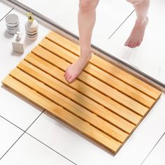 a person standing on a wooden mat in front of a shower door with their bare feet