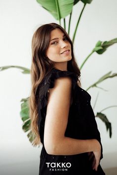 a woman standing in front of a plant with her hands on her hips and looking off to the side