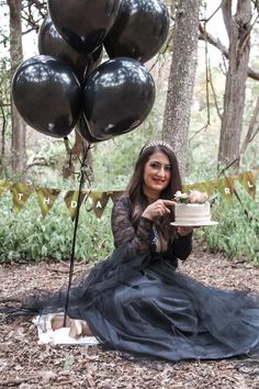 a woman sitting on the ground holding a piece of cake in front of some balloons