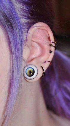 a woman with purple hair has an eyeball shaped earring on her left side