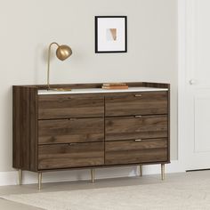 a wooden dresser sitting next to a white wall with a framed picture on top of it