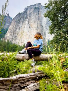 a woman sitting on top of a log in the woods next to a large mountain