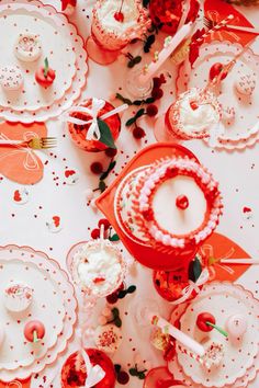 a table topped with lots of red and white plates covered in frosted cake next to cupcakes