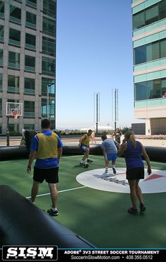 several people are playing tennis on an artificial court in front of a large glass building