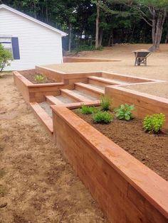 a wooden garden bed sitting on top of a dirt field next to a white house