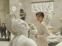 a woman standing next to a white statue in a room filled with statues and sculptures