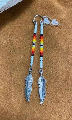 two pairs of earrings with colorful beads and feathers hanging from hooks on a brown surface