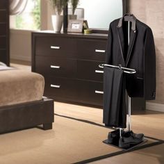 a suit and tie hanger on a stand in front of a bed with a large mirror