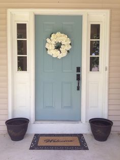 a blue front door with two flower pots and a welcome mat