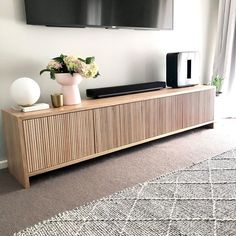 a tv mounted on the wall above a wooden cabinet with vases and flowers in front of it