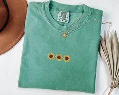 a green t - shirt with sunflowers embroidered on the front, and a straw hat next to it