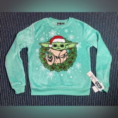 a baby yoda wearing a santa hat on top of a green sweater with snowflakes