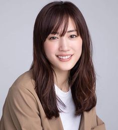 a woman with long brown hair smiling at the camera and wearing a tan blazer