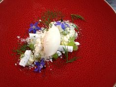 a red plate topped with food and garnished with blue flowers on the side