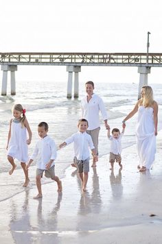 a family walking on the beach holding hands and smiling at the camera with pier in background