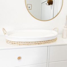 a white dresser with a round mirror and wicker basket on the top, in front of it