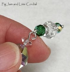 a person is holding a tiny green and white beaded charm on their finger,