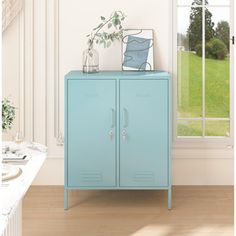 a blue cabinet sitting in front of a window next to a table with a potted plant