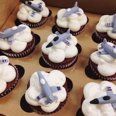 cupcakes with white frosting and airplanes on them in a cardboard box, ready to be eaten