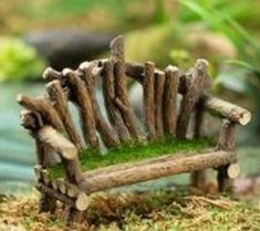 a miniature wooden bench made out of sticks and moss sitting on the ground in front of a pond