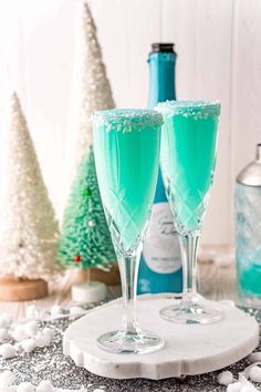 two glasses filled with green liquid sitting on top of a white plate next to christmas trees