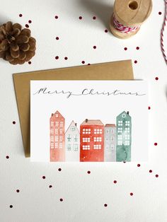 a christmas card with watercolor buildings on it next to a spool of twine