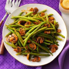 a white plate topped with green beans covered in mushrooms next to a fork and knife