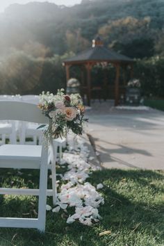 a white chair sitting on top of a grass covered field next to flowers and a gazebo