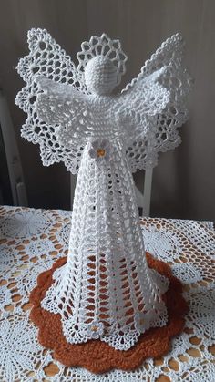 a crocheted angel sitting on top of a doily covered table with an orange and white place mat