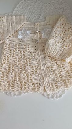 a white crocheted sweater with buttons on the collar and sleeves is laying on a table