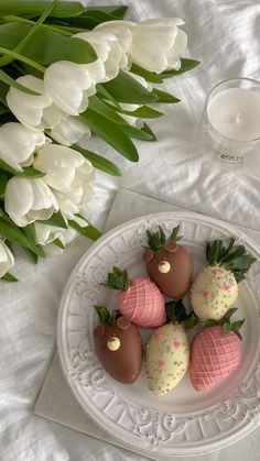 chocolate covered strawberries on a white plate next to tulips and a candle