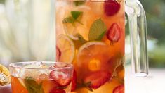 a pitcher filled with fruit and ice next to a glass full of lemonade on a table