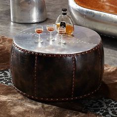 a leather ottoman with three wine glasses on it and a bottle of alcohol in the middle