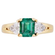 GIA-certified 1.30-carat natural minor oil emerald and trillion cut diamond 3-stone ring in 18 karat solid yellow gold. The emerald center stone features excellent clarity, transparency, and luster. The stone's impressive color and clarity is all the more impressive considering the minor oil treatment. Flanked by 2 near-flawless trillion-cut diamond side stones that offer excellent aesthetic contrast and symmetry. 3-stone rings symbolize the past, present, and future. The ideal statement or engagement ring for her. Emerald Details: - Species: Natural Beryl - Variety: Emerald - Geographic Origin: Zambia - Measurements: 7.12 x 5.60 x 4.33 mm - Shape: Octagonal - Cutting Style: Step Cut - Transparency: Transparent - Color: Green - TREATMENT(S): Minor (F1) Ring Details: - Weight: 5.94 grams (g Wide Band Engagement Ring, Trillion Diamonds, Art Nouveau Ring, Engagement Ring For Her, 3 Stone Rings, Stone Feature, Zambian Emerald, 18k Gold Ring, Gold Band Ring