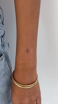 a woman's arm with a tiny star tattoo on it and a gold bracelet