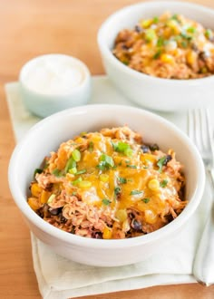 two white bowls filled with food on top of a wooden table next to a fork