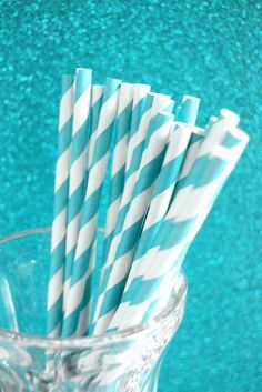 several striped paper straws in a clear glass cup on a table with green background