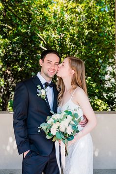 a bride and groom kissing in front of trees