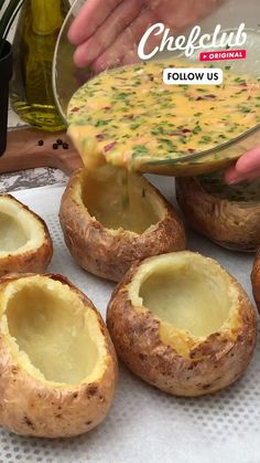 baked potatoes with cheese being drizzled over them by a person's hand