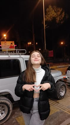 a young woman standing in front of a white truck at night with her hands together