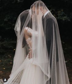 a bride and groom kissing in front of some trees with their veils pulled back