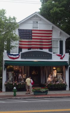 two people standing in front of a shop with an american flag on the roof and windows